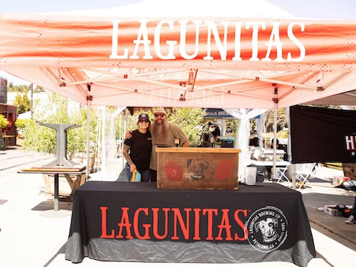 Two people standing behind a Lagunitas Brewing Co. branded table with a large 'Lagunitas' sign above.