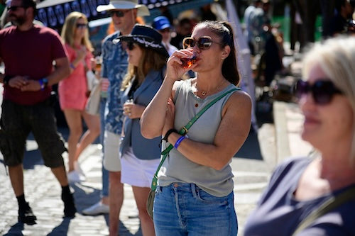 Woman drinking a craft beer from a glass in a busy outdoor setting