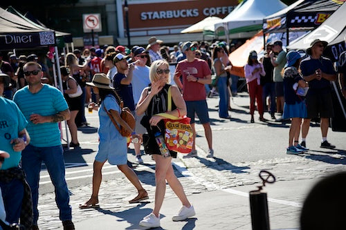 Woman strolling through the event holding a the Designated Driver goodie bag in a bustling street scene with people and tents.