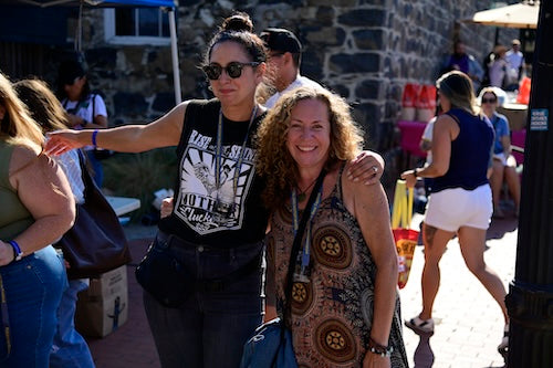 Two women posing for a photo at the Beer Fest with people and umbrellas in the background.