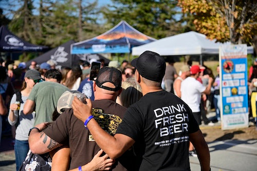 People at the Craft Beer Fest with beer tents in the background and a person wearing a 'Drink Fresh Beer' shirt.