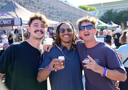 Three men posing together at the Petaluma Craft Beer Fest event, holding craft beer.