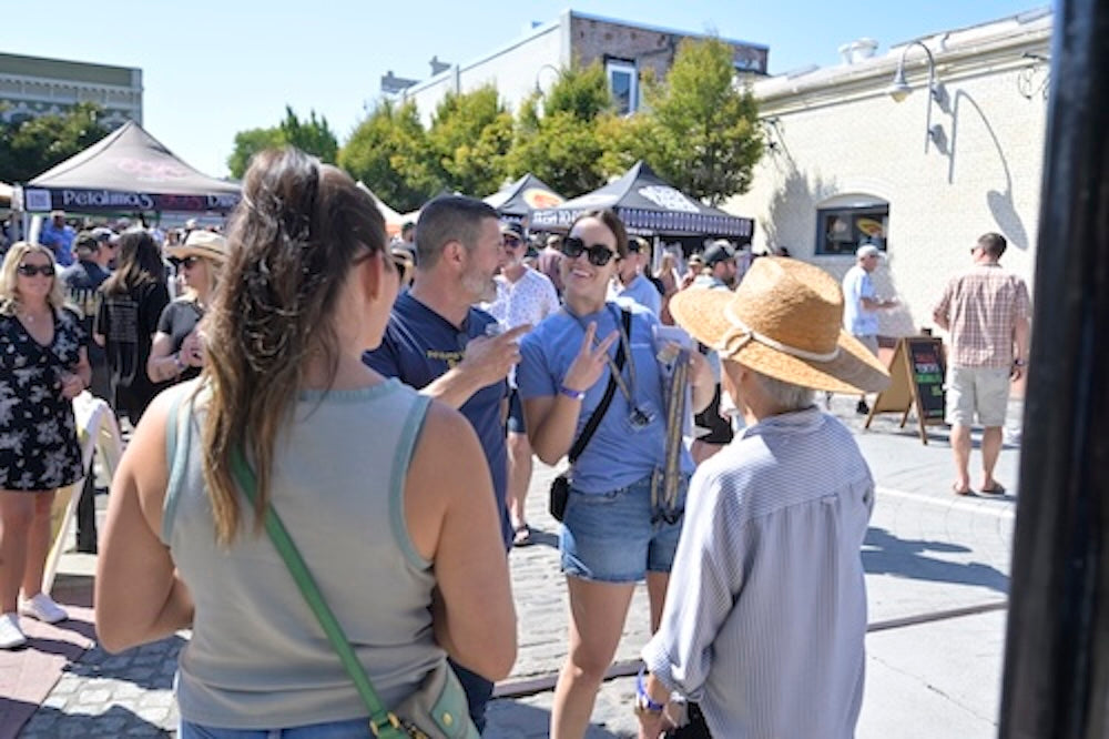Happy people outdoors on a sunny day with beer fest food tents and buildings in the background.