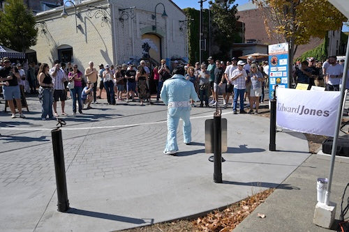 Group of people gathered watching "Elvis" perform in costume with a building in the background and with a 'Edwards Jones' sign to the right.