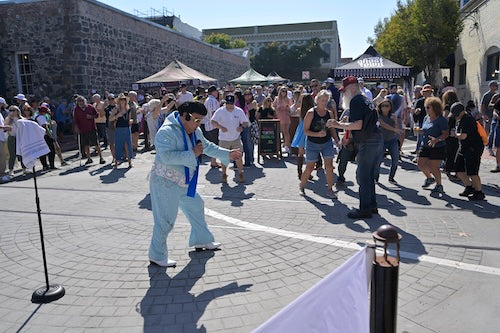 Elvis is in the house!  Elvis impersonator singing in the street with fans gathered and some dancing.