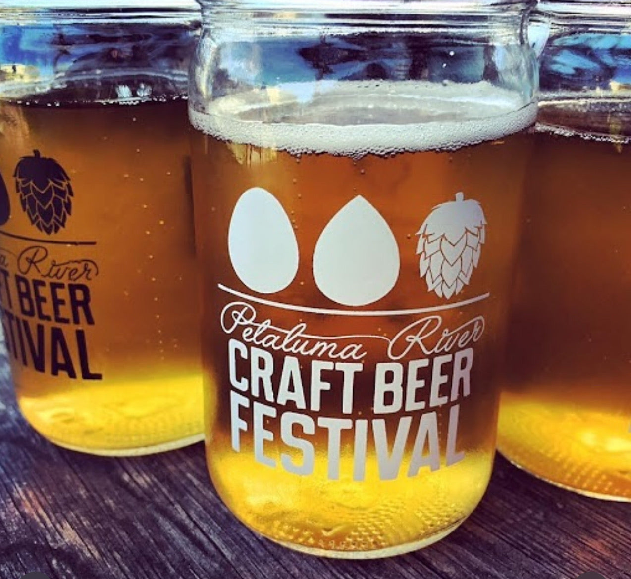 Mason jar filled with beer from Petaluma River Craft Beer Festival on a wooden surface.
