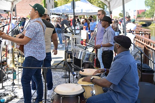 Street musicians playing drums and guitar in at the beer fest band tent and people in the background watching.