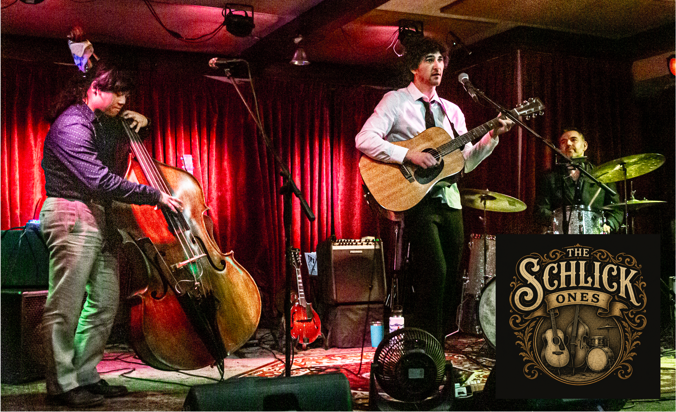 Live band performance on stage with a double bass, acoustic guitar, and drums under red curtains. A large 'The Schlick Ones' logo overlay is visible in the bottom right corner.